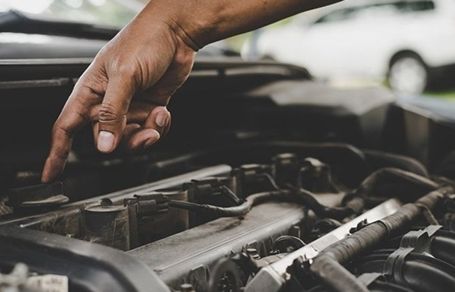 Close-up of technician working on components inside a car engine bay.