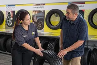 A technician using a flashlight to inspect the brakes on a vehicle.