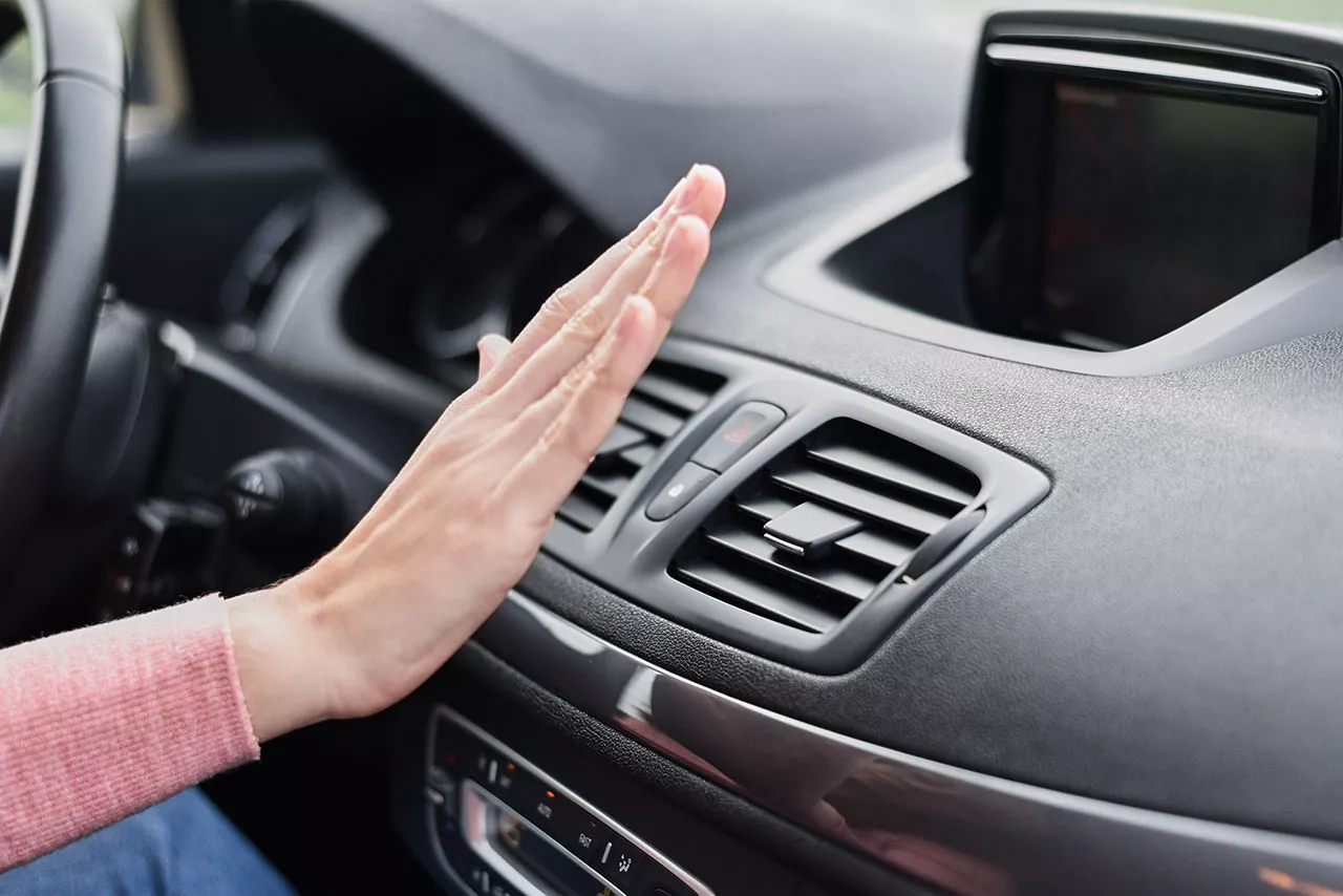 Driver holding their hand up to air conditioning vents to feel for air.