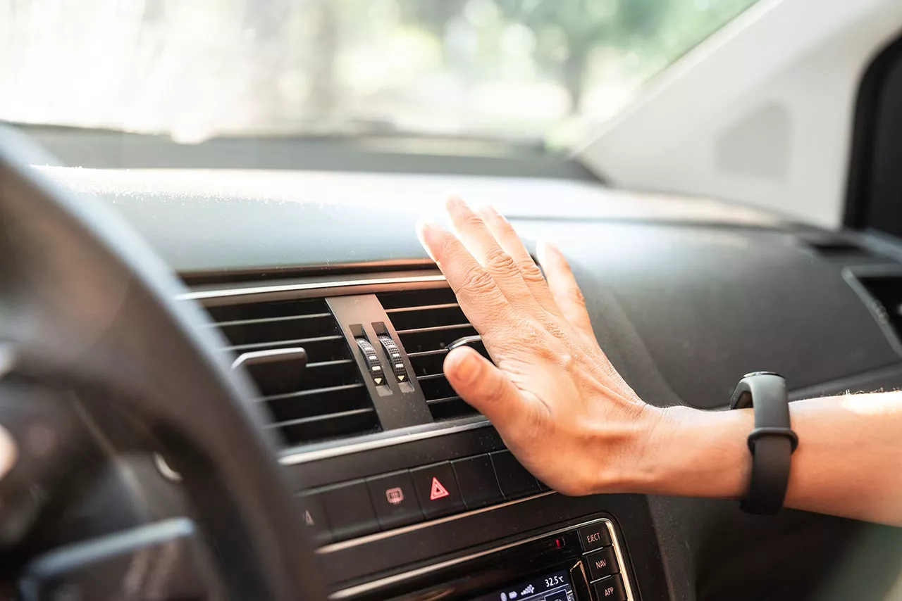 Driver holding their hand up to air conditioning vents to feel for air.
