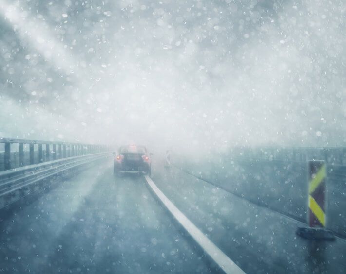 Car driving in winter weather, limited visual distance, and snow falling on roadway