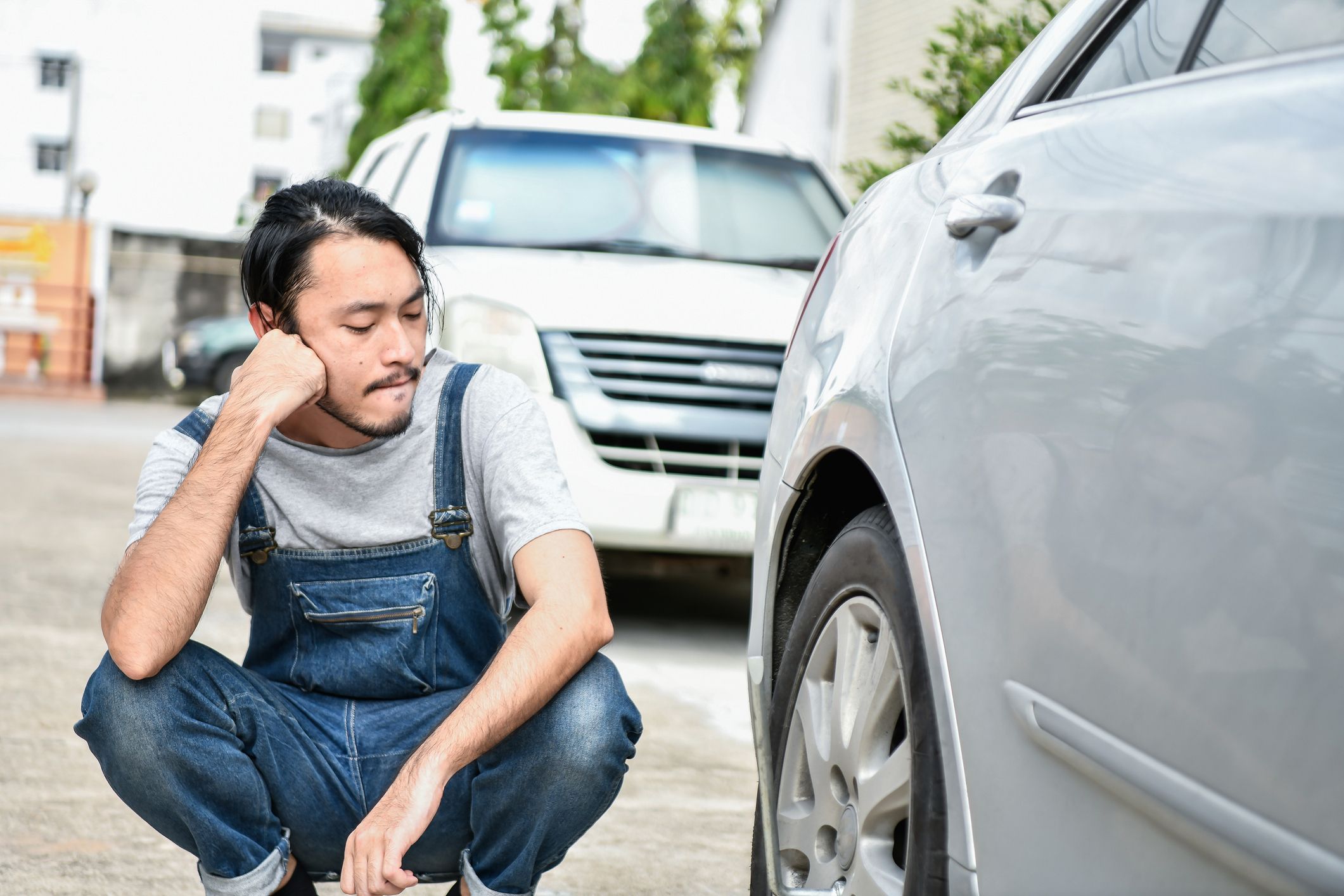 Man looking at flat tire of car, sitting on floor