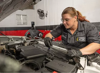 A technician closely inspecting a car engine bay with a flashlight.