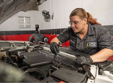 A technician closely inspecting a car engine bay with a flashlight.