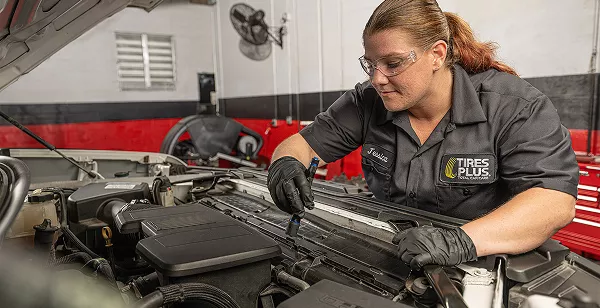 A technician closely inspecting a car engine bay with a flashlight.