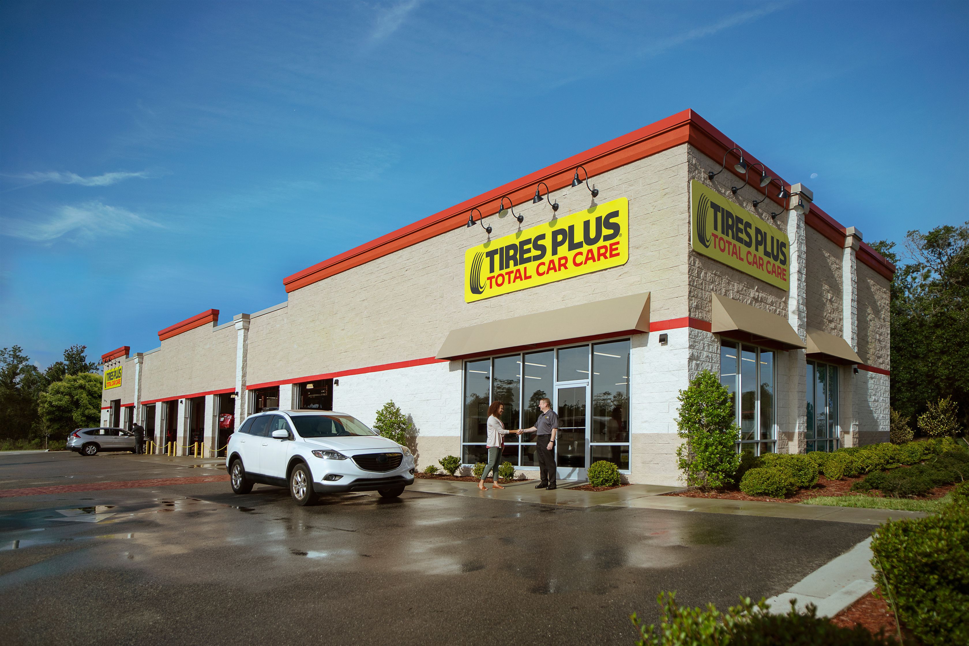 A Tires Plus advisor and customer shaking hands outside of a Tires Plus Total Car Care storefront. 