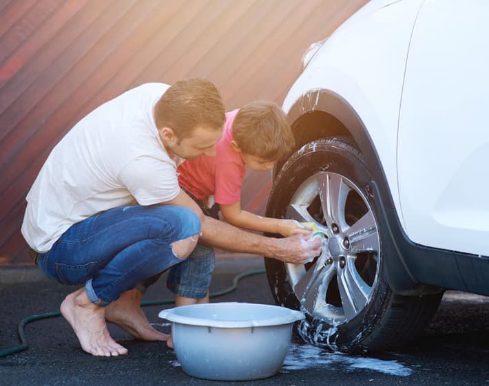 Father and son cleaning car tire together.