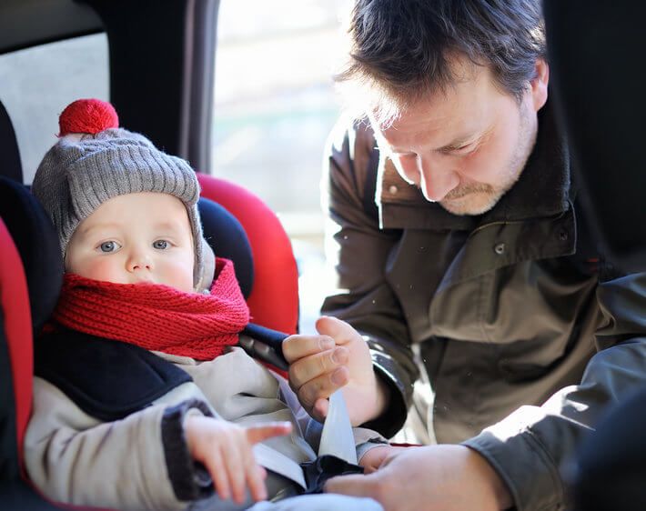 father securing baby in car seat