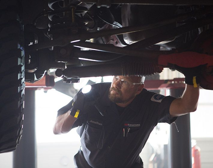 Firestone Complete Auto Care technician examining undercarriage of car