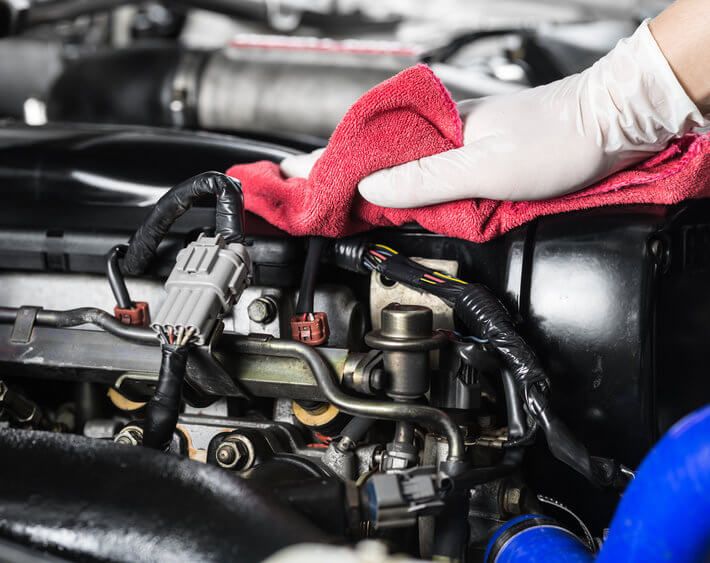 Gloved hand cleaning car engine with red cloth