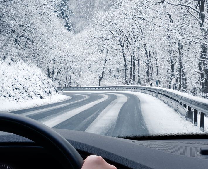 Driver's hands gripping steering wheel on snowy road, surrounded by snow covered trees