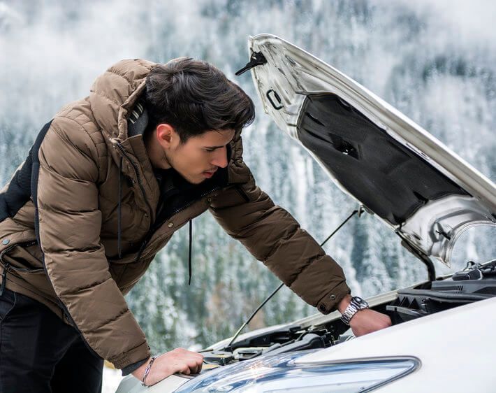 guy wearing a brown coat checking a car battery in winter