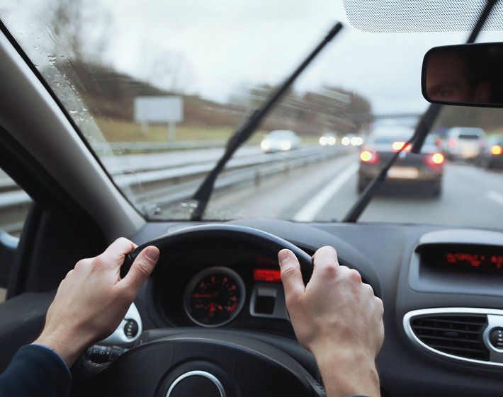 Driving in wet road conditions, driver's hands on steering wheel and windshield wipers moving