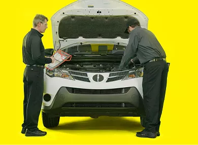 Two auto technicians checking under the hood of a SUV.