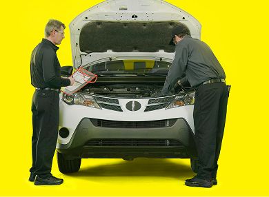Two auto technicians checking under the hood of a SUV.
