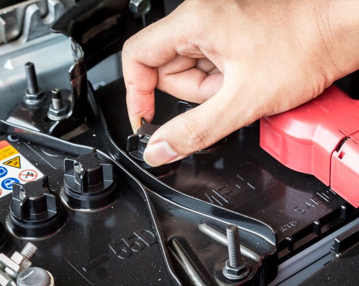 Hand on car battery, checking terminal connections