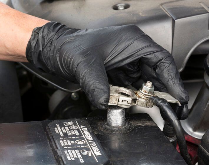 Gloved hand removing car battery terminal to clean the battery