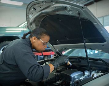 auto technician using flashlight to check engine under the hood