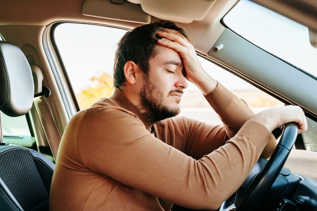 Side view young male driver closed his eyes and rests with his hand on the steering wheel and the other on his forehead. To work productively, you need to have a good rest. The guy is tired.