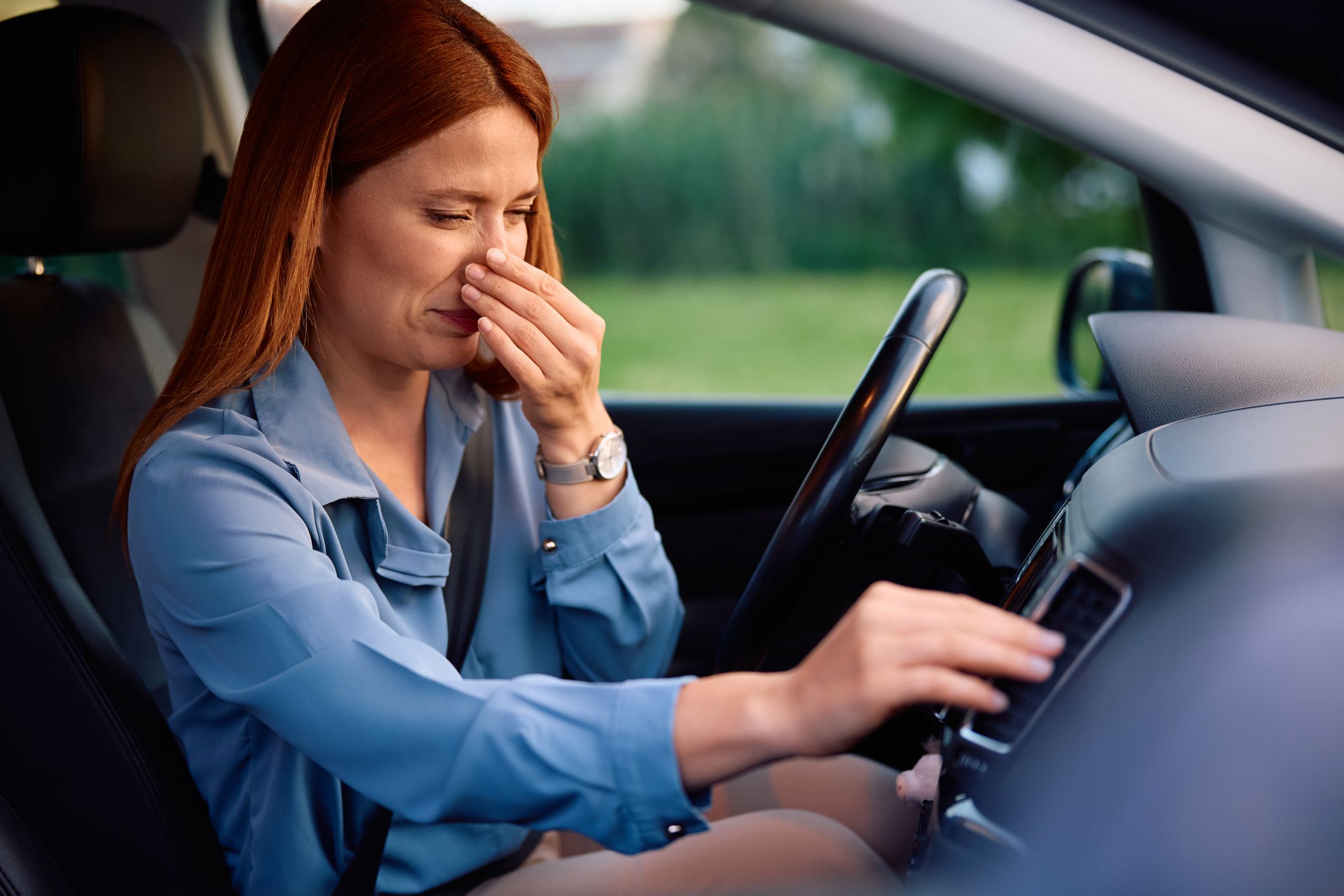 Woman holding her nose in a car due to a foul smell