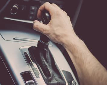 Male hand gripping gear shifter of vehicle