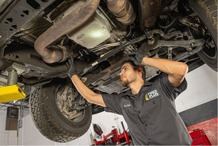 An expert technician works under the chassis of a car.