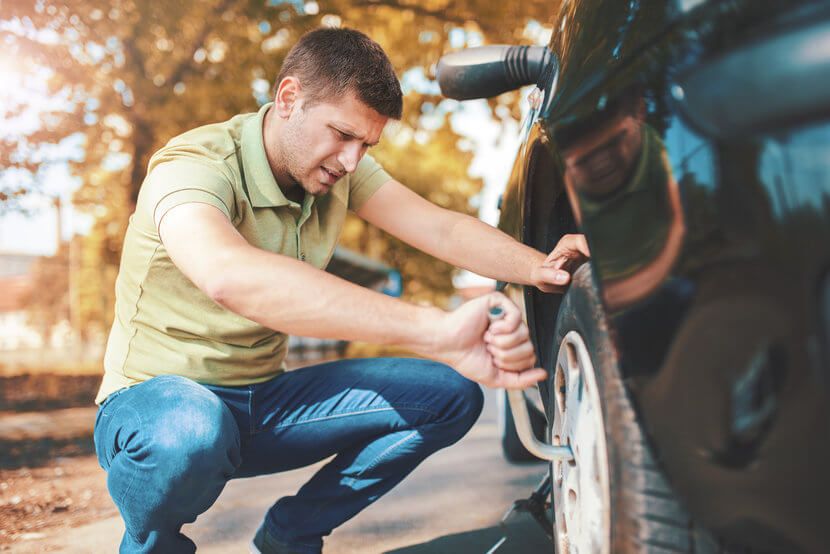 Man in green polo changing a flat tire on the side of the road