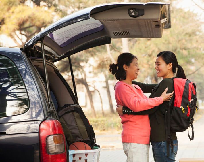 Mother and daughter hug goodbye outside of their car as daughter leaves for college