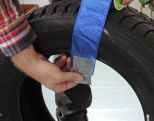 Wrapping ribbon around old tire to transform it into a giant holiday ornament