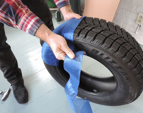 Continuing to wrap blue ribbon around used tire to transform it into a giant holiday ornament decoration