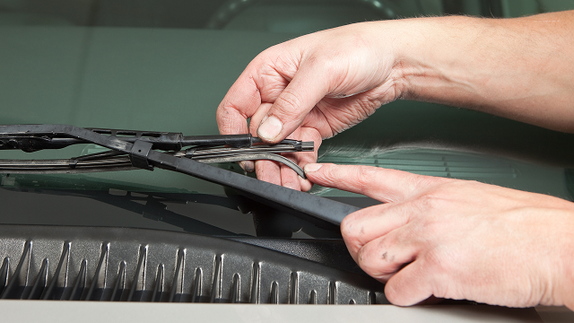 A pair of hands manipulating a worn-out wiper blade.