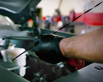 Person with black gloves cleaning dip stick with red rag.