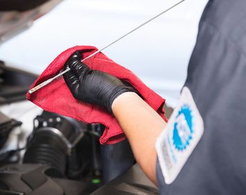 person standing in front of car engine cleaning oil dipstick with red rag