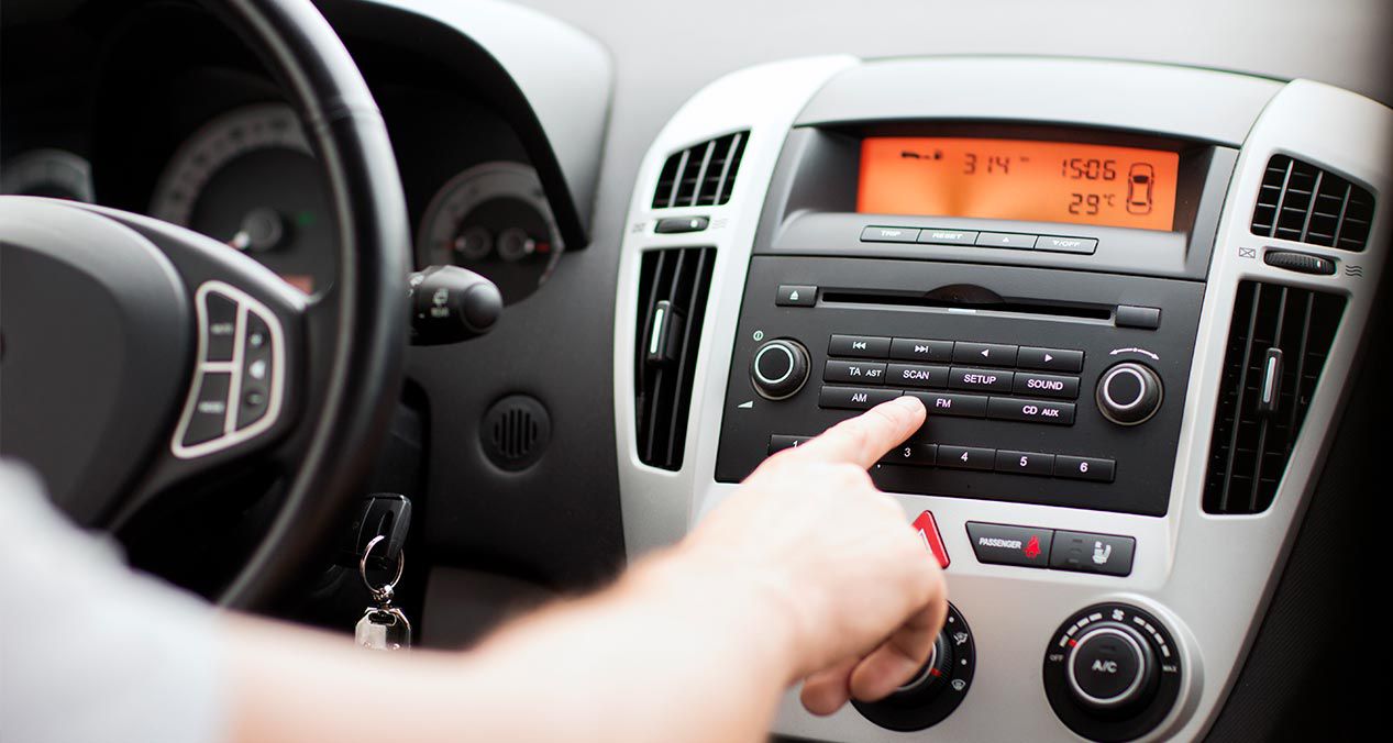 tablero de un auto con la radio encendida y una mano cambiando de frecuencia