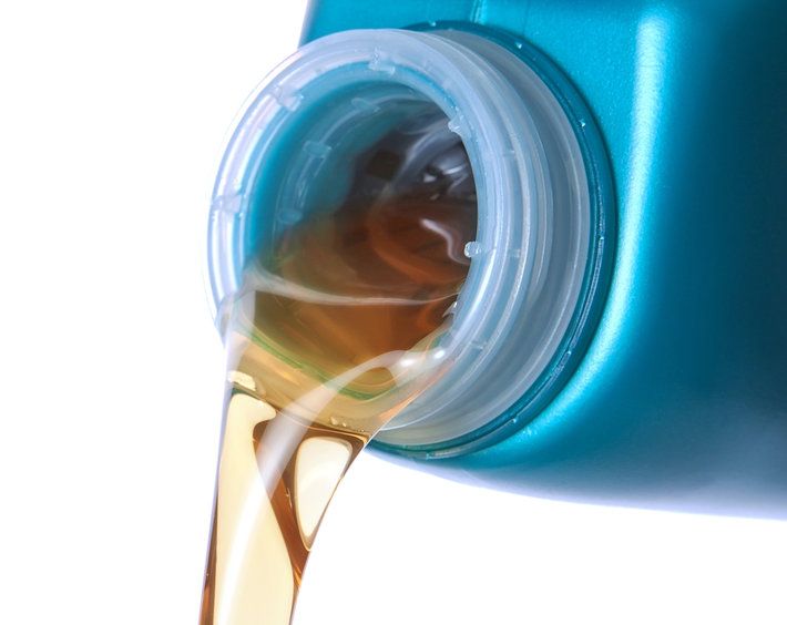 Close up of new motor oil being poured from blue container, on white background