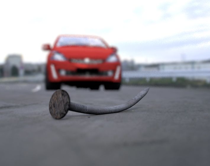 Red car approaching nail in road, safe driving tips from Firestone Complete Auto Care