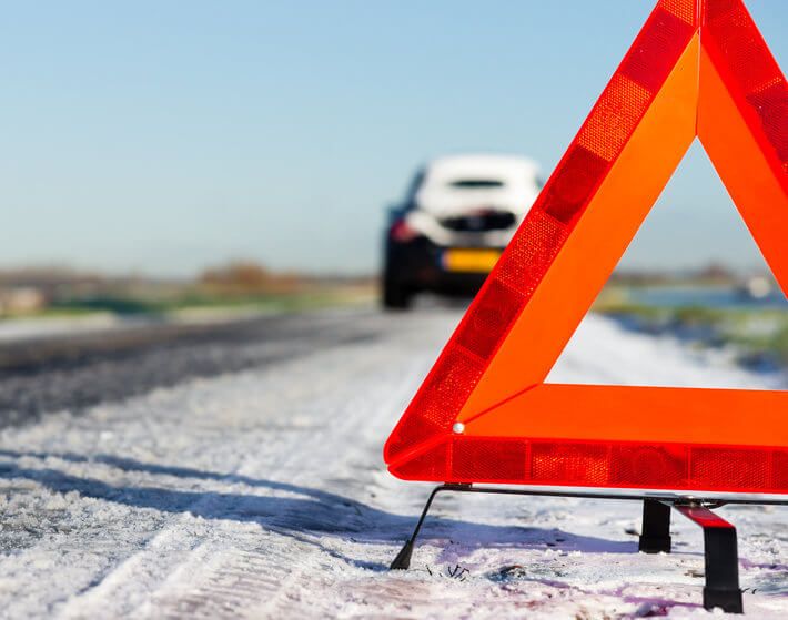 Close up of orange hazard triangle on snowy road, car in background