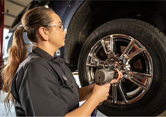 Technician adjusting fasteners on a wheel of an elevated vehicle.