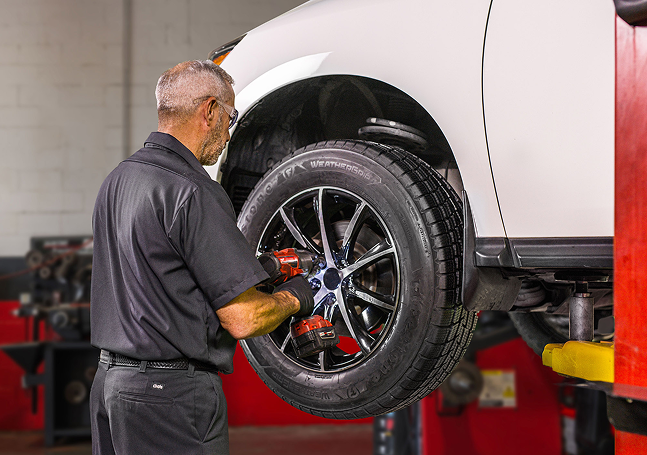 A technician adjusting fasteners on the wheel of a vehicle in an auto shop.