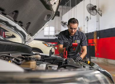 A technician uses a diagnostic tool to test a vehicle's battery in a Tires Plus auto repair shop.