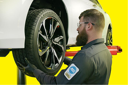 A technician using a flashlight to inspect the brakes on a vehicle.