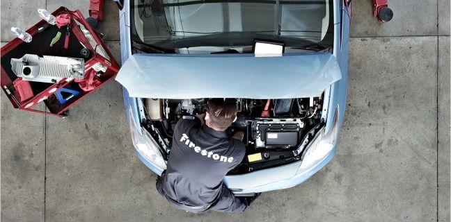 Overhead view of a Firestone technician working under the hood of a car.