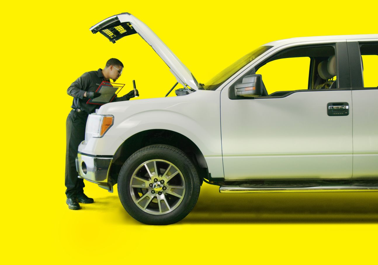 An auto technician checking under the hood of a SUV.