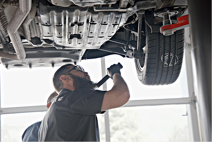 Technician using a flashlight to look at a tire of a raised car.