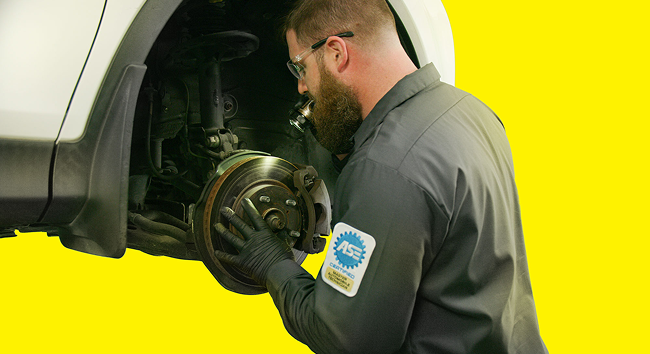A technician inspecting brake components with a flashlight.