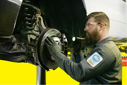 A technician using a flashlight to inspect the brakes on a vehicle.