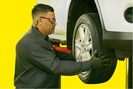 A technician installing a tire on a vehicle raised up on a hydraulic lift.