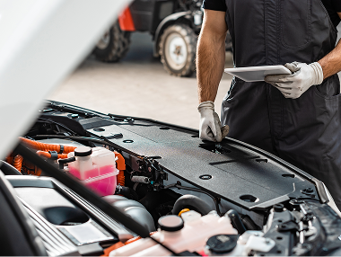 Technician looking at a tablet while working under the hood of a car.