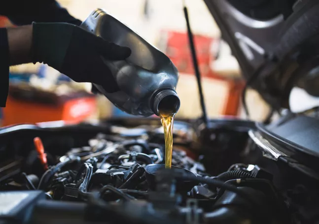 An auto technician pouring motor oil into the top of a car engine.