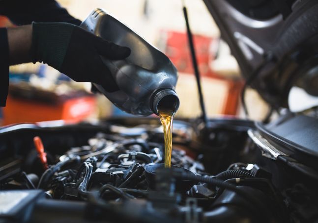 An auto technician pouring motor oil into the top of a car engine.